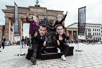 Berlin vor dem Brandenburger Tor: Aktive verkleidet als Merkel, Macron und May vor dem „Waffenthron“, bestehend aus Nachbildungen von Kleinwaffen